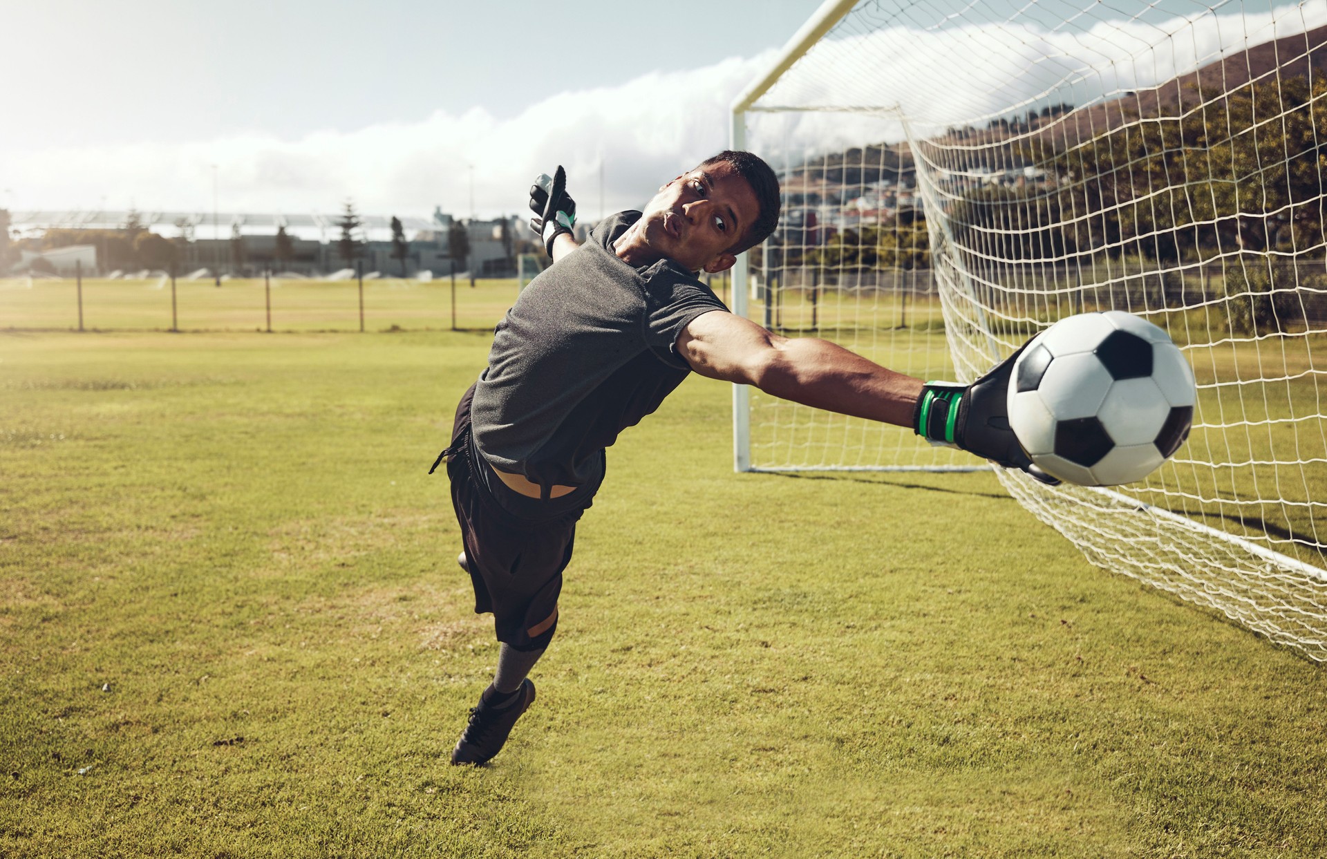 Soccer, sports and goalkeeper training on a field for a professional competition. Young and strong athlete with energy and motivation catching a football during a game or exercise on a sport ground